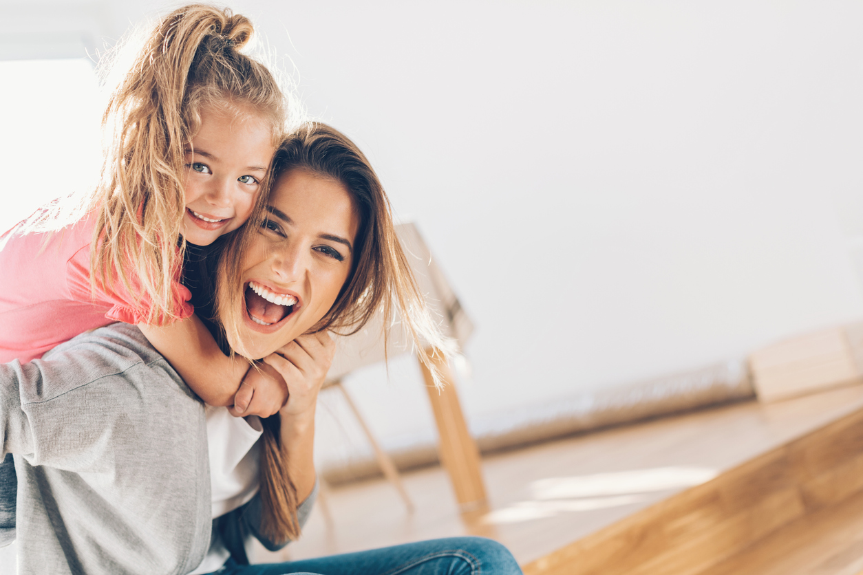 A young mom smiles broadly while being hugged by her daughter