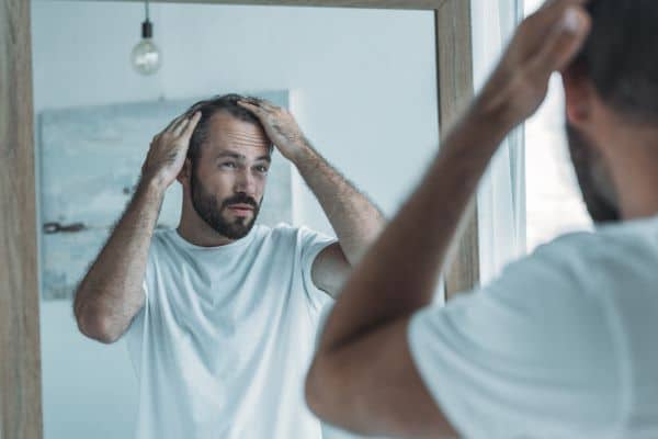 A middle age man looks in the mirror and examines his thinning hair with his hands