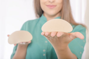 woman holding two different types of breast implants