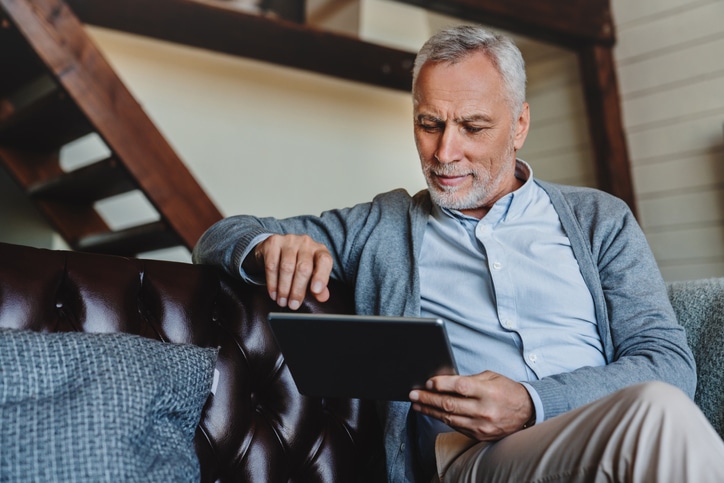 Middle-aged caucasian man websurfing on digital tablet at home.