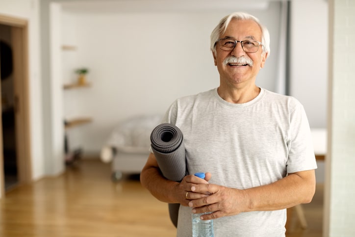 An elderly man holding a yoga mat and a bottle of water.
