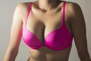 close up of woman's breasts wearing a pink bra against grey background