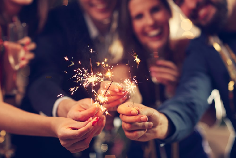 A close up of a group of friends on New Year's Eve laughing and holding their sparklers together