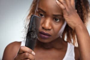 Stressed woman looking at comb that has hair on it, dealing with hair loss.