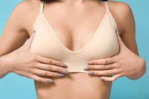 Close up of a woman holding her breasts in a nude bra to show that she wants to get a breast lift.