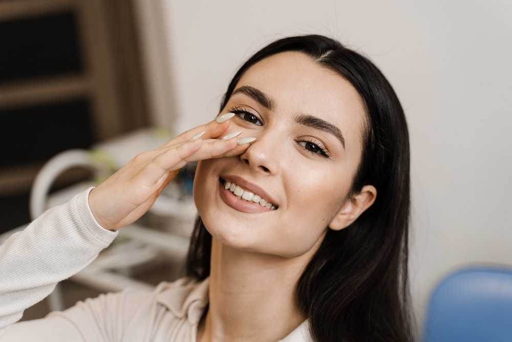 Woman smiling and touching her nose after rhinoplasty in Dallas, TX